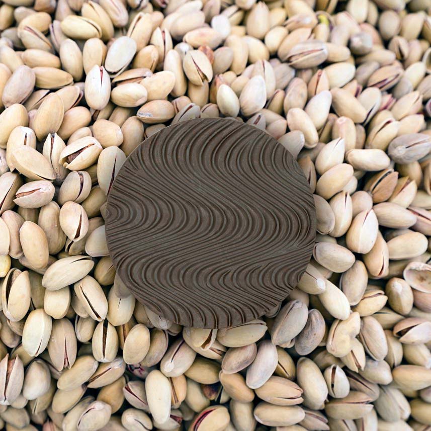 Dark Keto Chocolate bar piece with wavy designs sitting on whole pistachios.