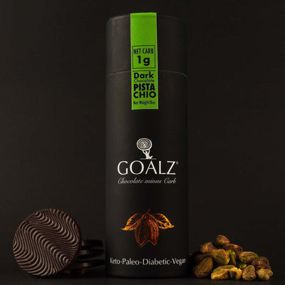 Allulose Sweetened Goalz Dark Chocolate with Pistachios and with 1g net carb per serving. The black chocolate canister standing next to shelled organic pistachios and sugar-free chocolate bars. The canister has a goalz logo and text that says Chocolate minus carb. There is a orange copper metallic cocoa pods with cocoa beans showing under the logo. At the bottom it says Keto, Paleo, Diabetic, and Vegan  