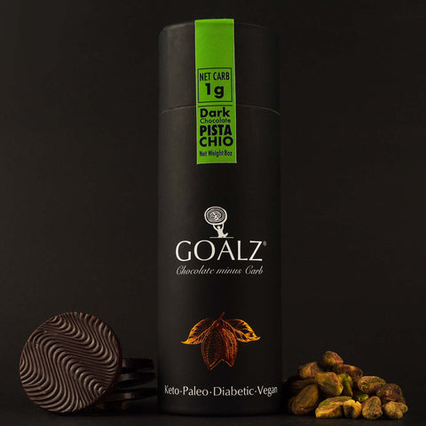 Allulose Sweetened Goalz Dark Chocolate with Pistachios and with 1g net carb per serving. The black chocolate canister standing next to shelled organic pistachios and sugar-free chocolate bars. The canister has a goalz logo and text that says Chocolate minus carb. There is a orange copper metallic cocoa pods with cocoa beans showing under the logo. At the bottom it says Keto, Paleo, Diabetic, and Vegan  
