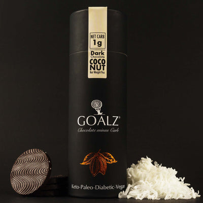 Allulose based dark chocolate with organic coconut flakes. White Goalz logo on a black box and text under logo that says Chocolate minus Carb. Chocolate discs are on the left and coconut shreds on the right