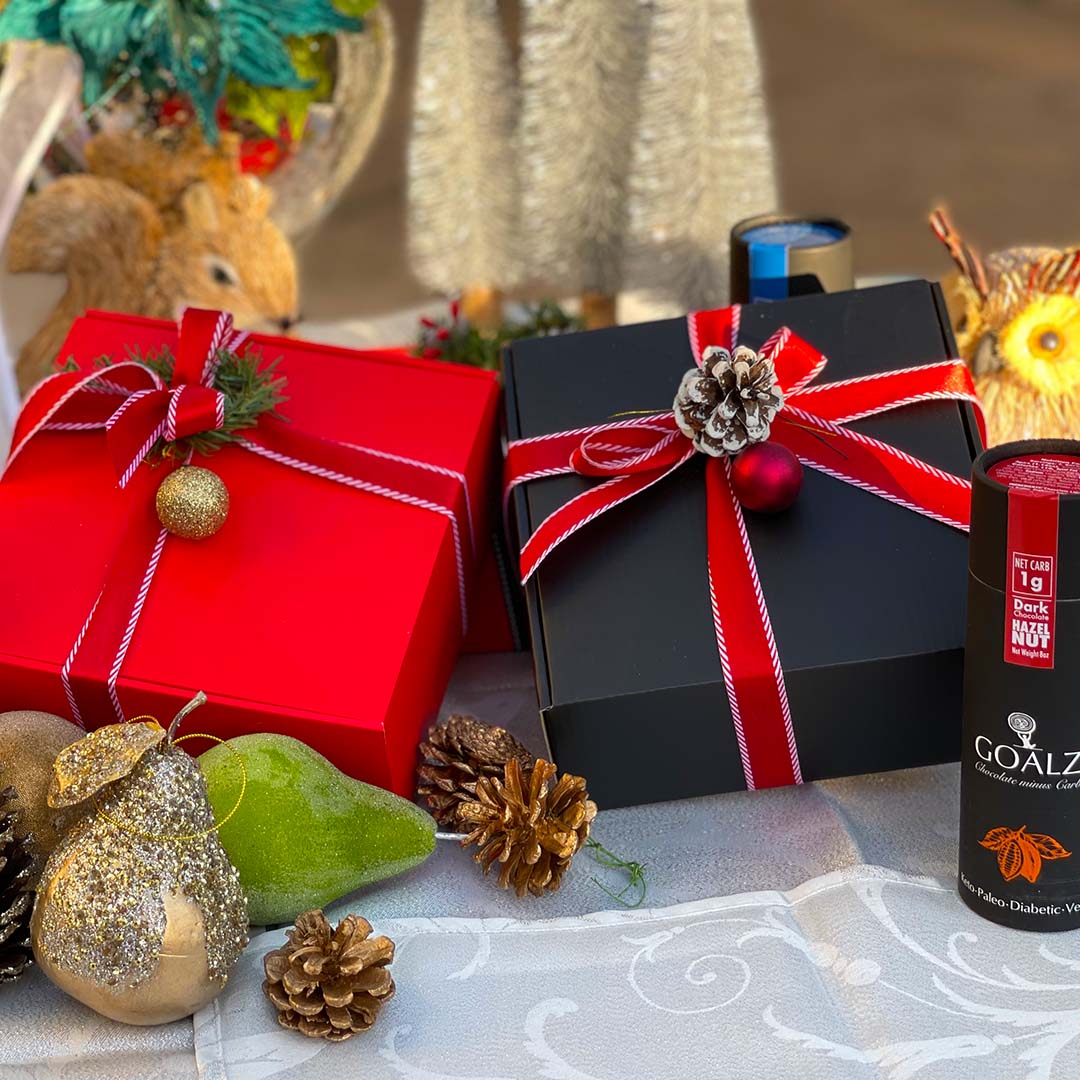 Black and Red Keto Chocolate gift boxes comes with your choice of low carb chocolates. Ribbon colors are red, gold, and white. There are Christmas decoration items  on the table